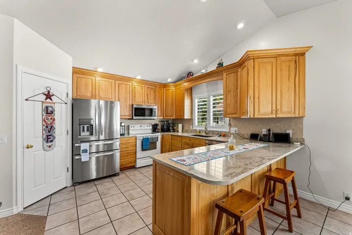 Kitchen featuring natural wood cabinetry, stainless steel appliances, a light-colored stone-finish countertop, and tile flooring