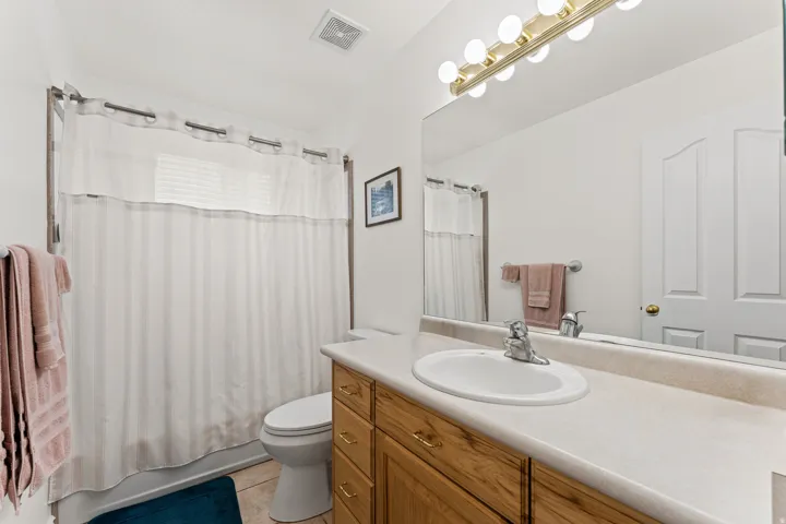 Bathroom featuring a single vanity with wood-finish cabinetry and a light-toned countertop, an integrated sink with chrome faucet, and a large wall-mounted mirror