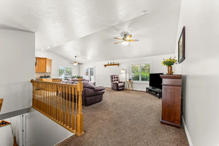 Carpeted living area featuring vaulted ceilings, a ceiling fan, and window shutters providing natural light