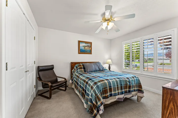 Bright room featuring a large window with white plantation shutters, a ceiling fan with integrated lighting, and a neutral carpet