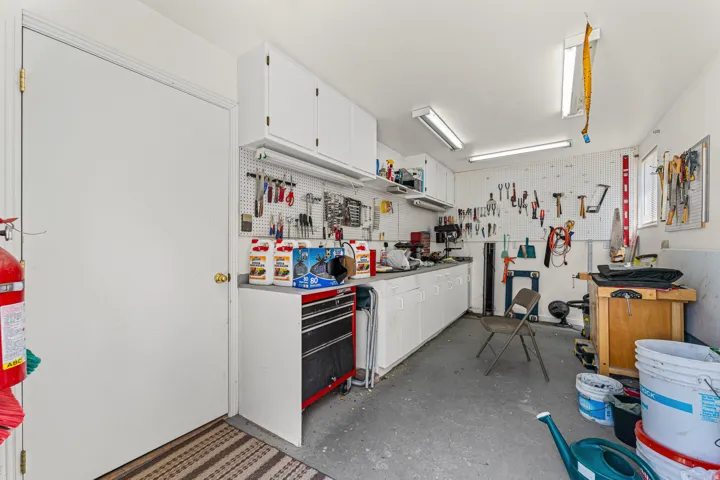 Garage work area featuring extensive pegboard storage, built-in lower cabinetry with countertop space, overhead fluorescent lighting, and a window for natural light
