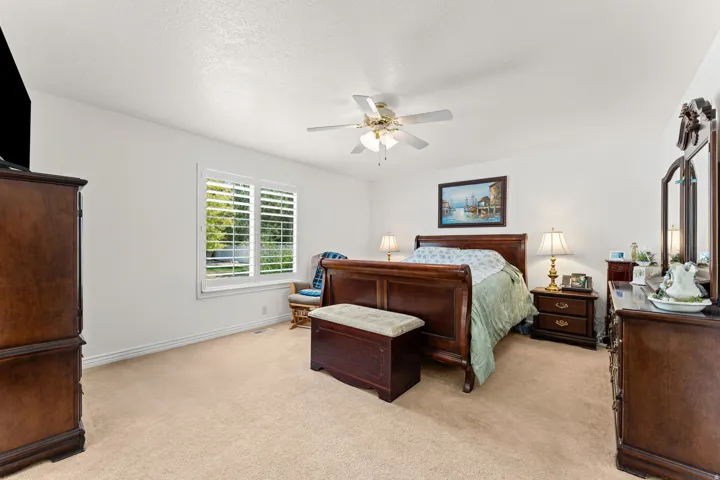 Carpeted bedroom with white walls, a ceiling fan, and a window with white louvered shutters