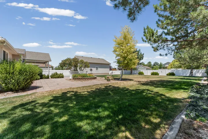 Expansive backyard featuring a lush lawn, mature trees, a stone paver patio, a raised garden bed, and a white privacy fence