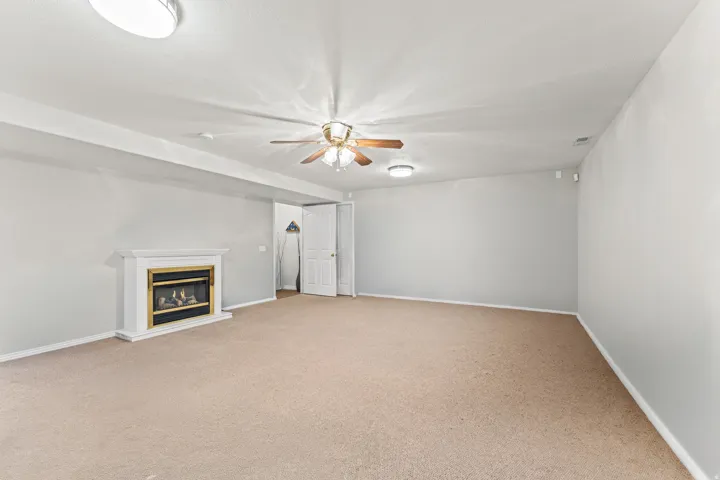 Spacious room featuring a white fireplace with a gold-toned insert, a ceiling fan with wooden blades, recessed lighting, and neutral-toned carpeting