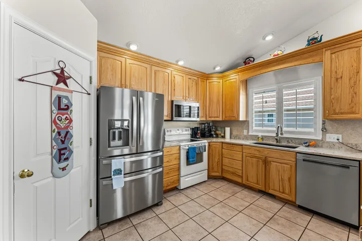 Kitchen featuring light wood cabinetry, stainless steel appliances, tile flooring, and a window with plantation shutters
