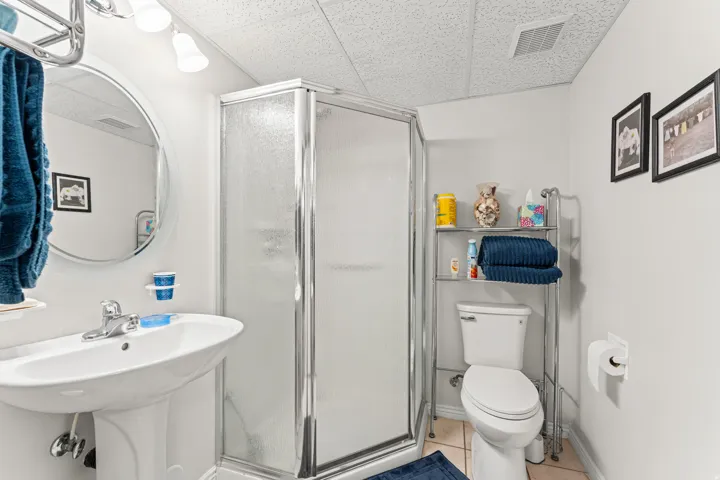 Bathroom featuring a pedestal sink, a glass-enclosed shower, and a commode
