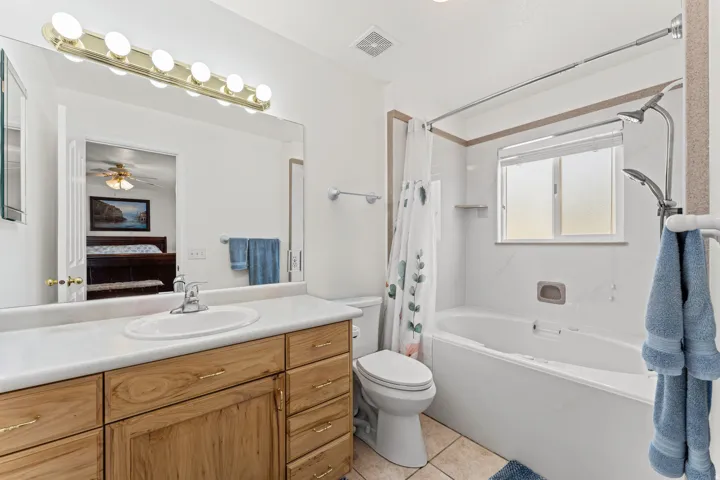 Full bathroom featuring a single vanity with wood cabinetry and a white countertop, a drop-in soaking tub with shower, and tiled flooring