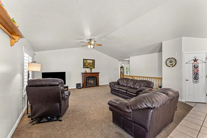 Spacious room featuring vaulted ceilings, a ceiling fan, and a wood-finish fireplace with mantel