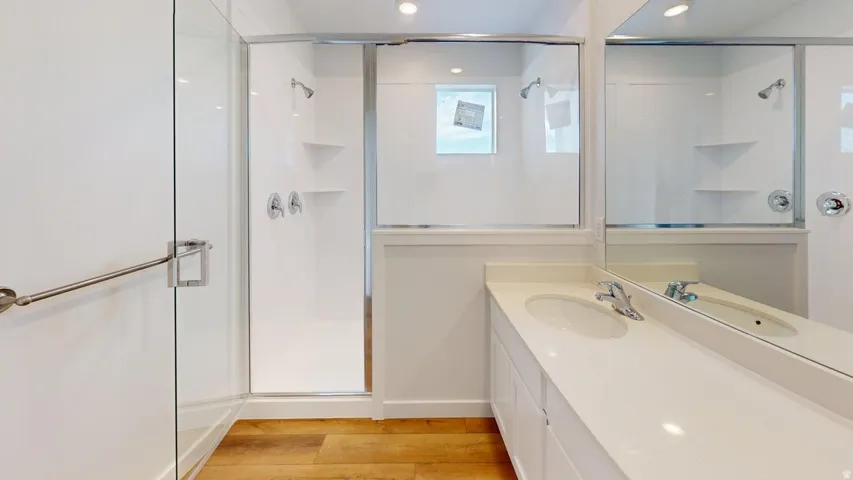 Modern bathroom featuring a double vanity with integrated sinks, a large mirror, and a glass-enclosed shower with a grab bar and built-in shelving