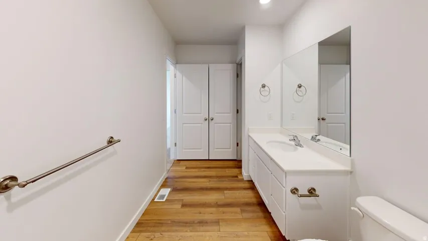 Bathroom featuring a white vanity with an integrated sink, a large wall-mounted mirror, and wood-finish flooring