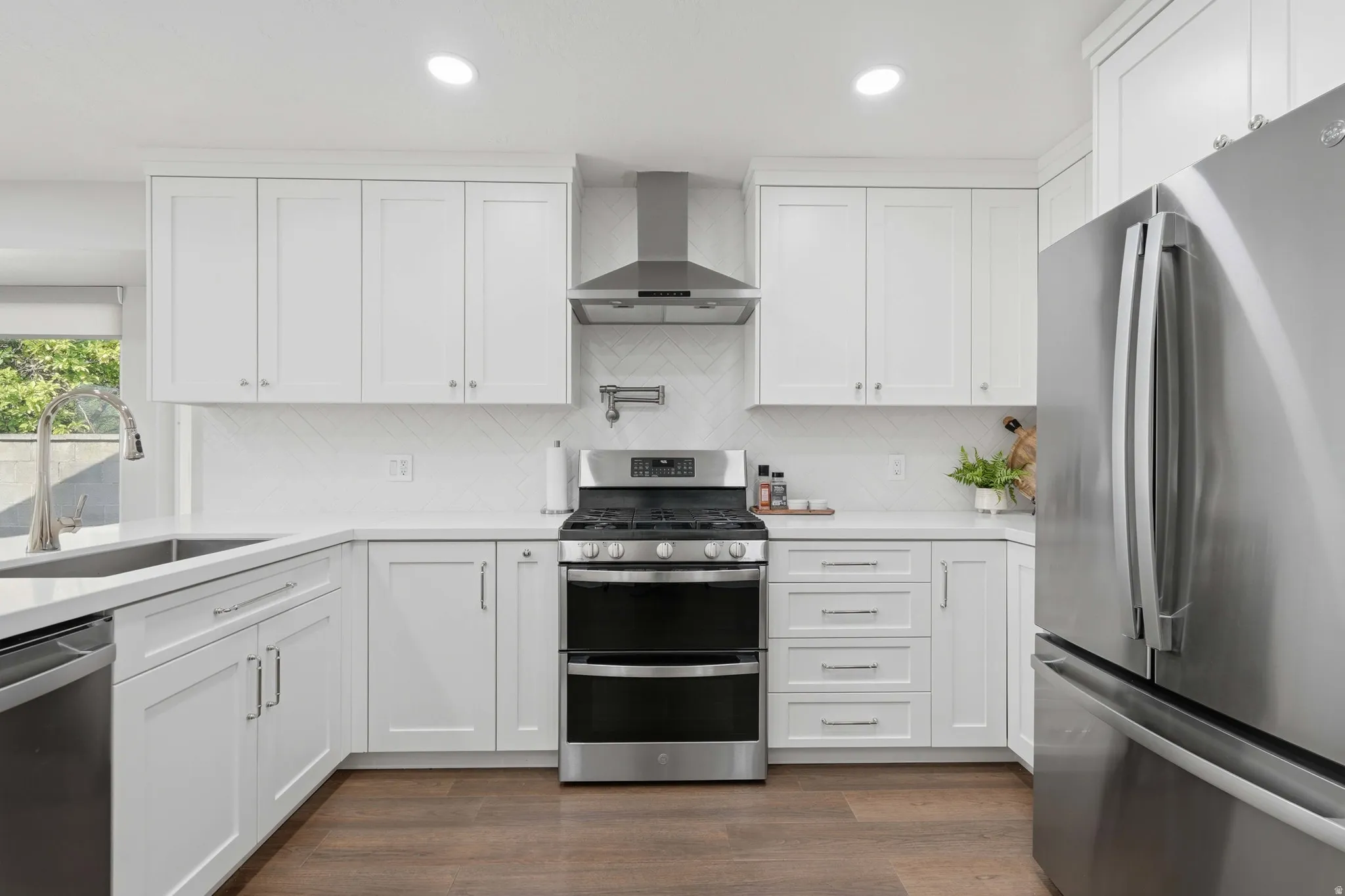 Modern kitchen featuring white shaker cabinetry, stainless steel appliances, white countertops, and a herringbone tile backsplash