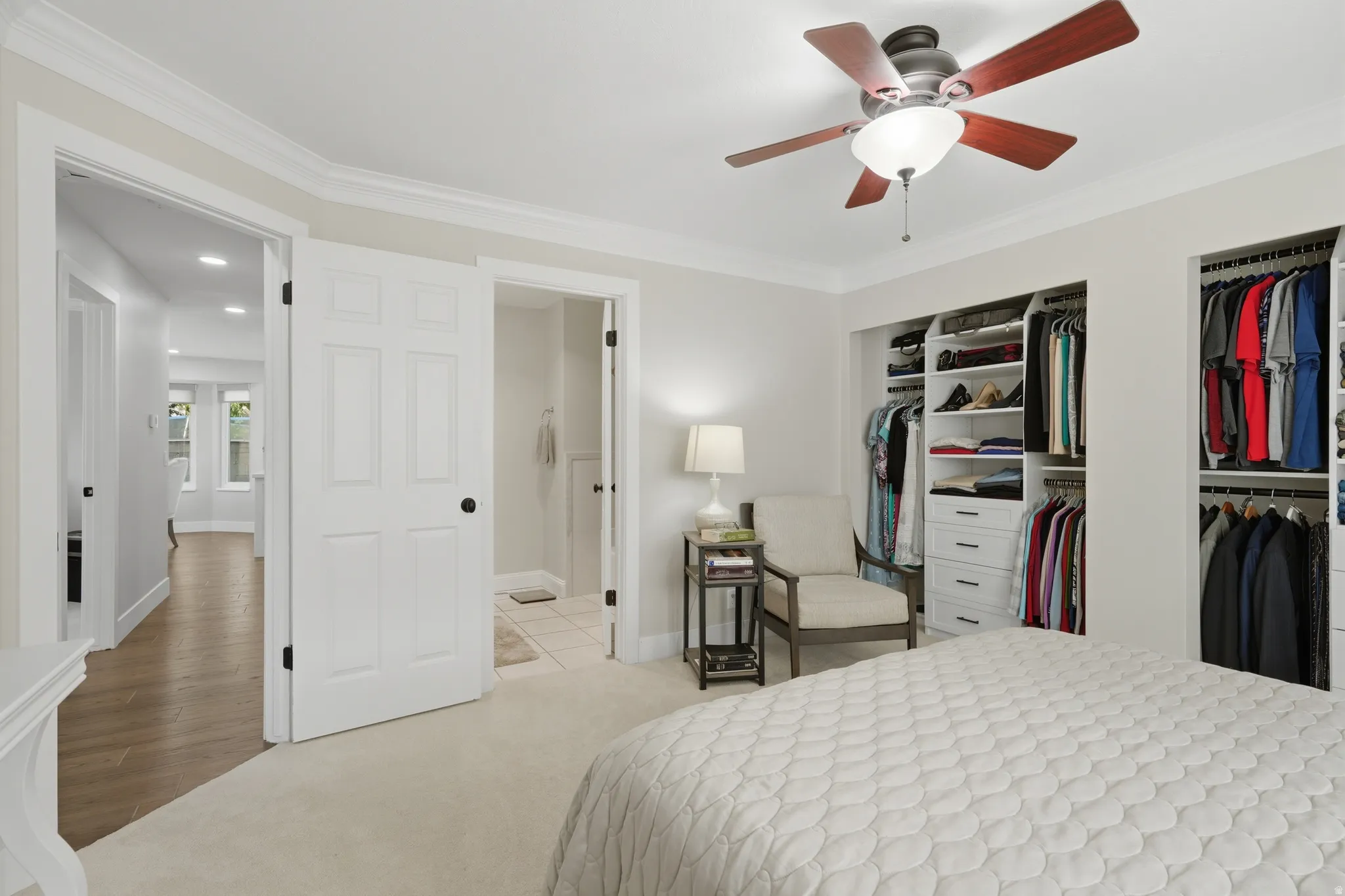 Bedroom featuring twin built-in closet systems with shelving and drawers, neutral carpeting, and a ceiling fan with light fixture