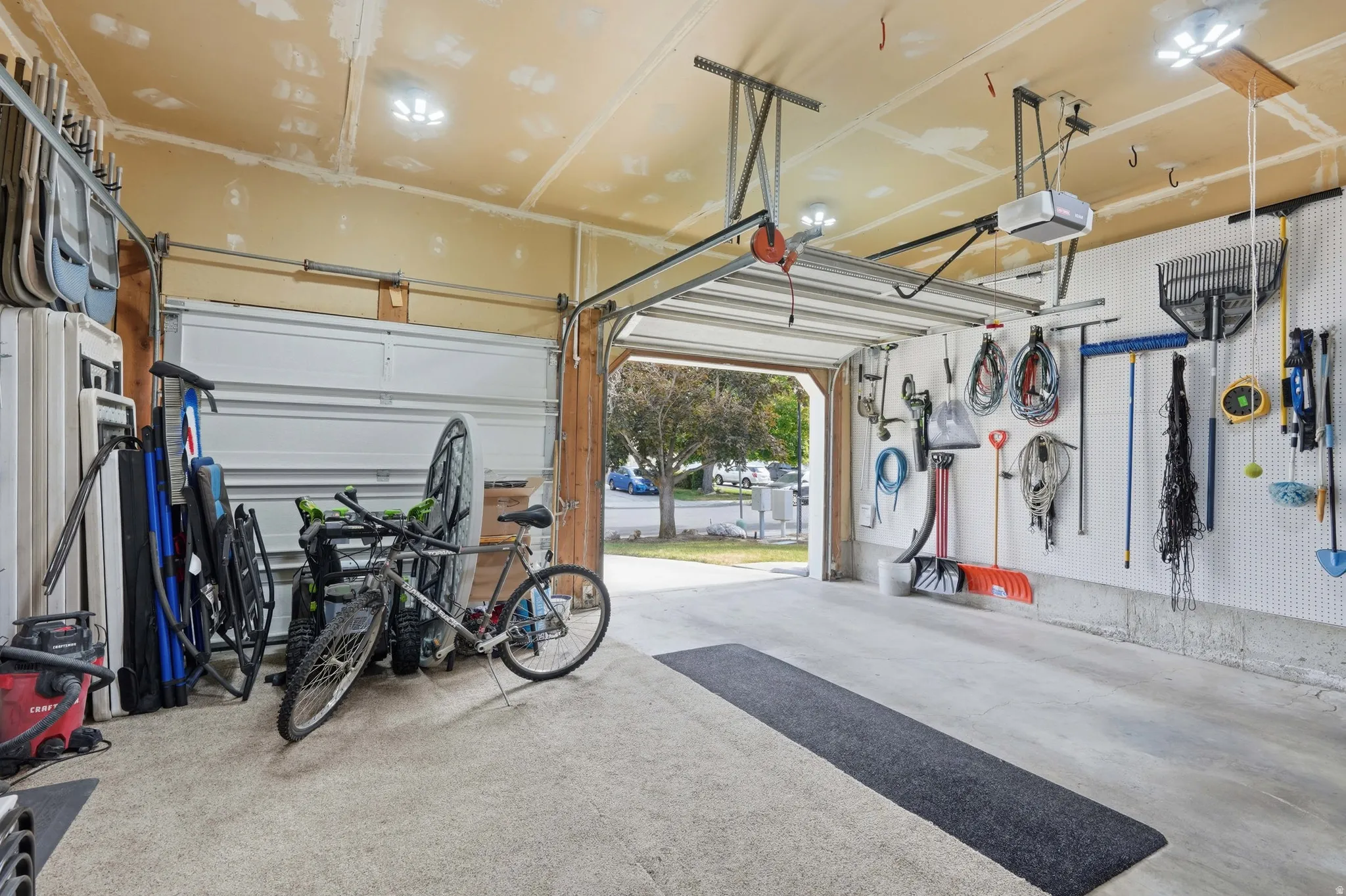 Spacious garage featuring two overhead doors, light-colored concrete flooring, and ample wall storage with pegboard organization