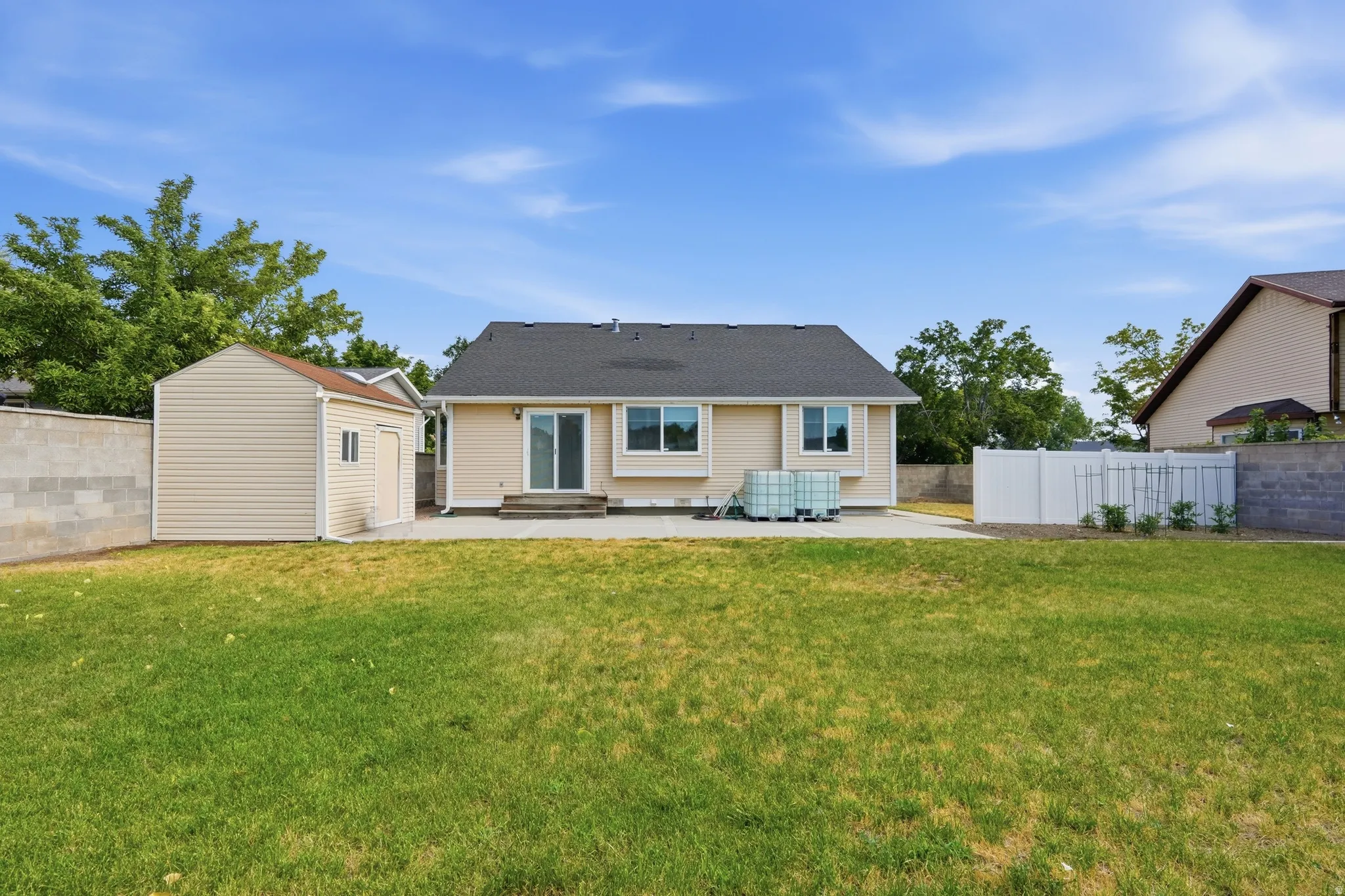 Expansive backyard featuring a large green space, a tan siding storage shed, a concrete patio, a sliding glass door entry, and a white privacy fence