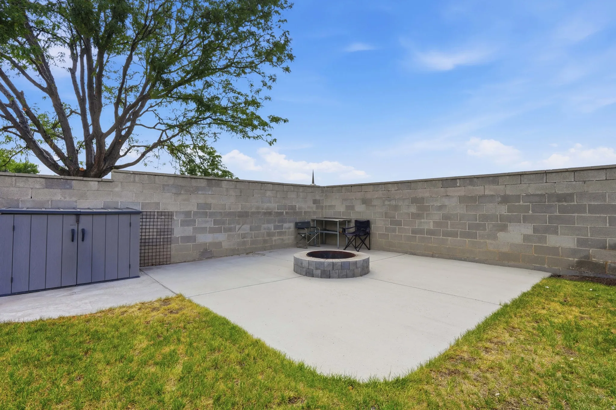 Outdoor patio featuring a built-in stone fire pit, concrete paver surface, and block wall perimeter