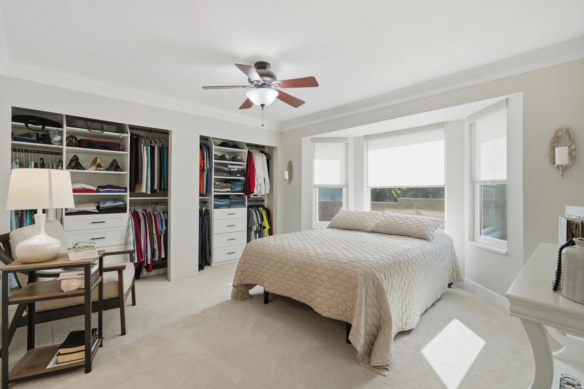 Bedroom featuring a bay window, recessed custom closet built-ins, light-toned carpeting, and a ceiling fan with integrated lighting