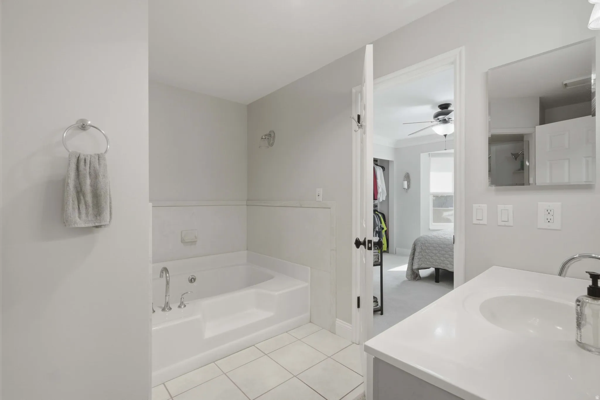 Bathroom featuring a built-in tub, tiled flooring, vanity with an integrated sink, wall-mounted mirror, and neutral wall paint