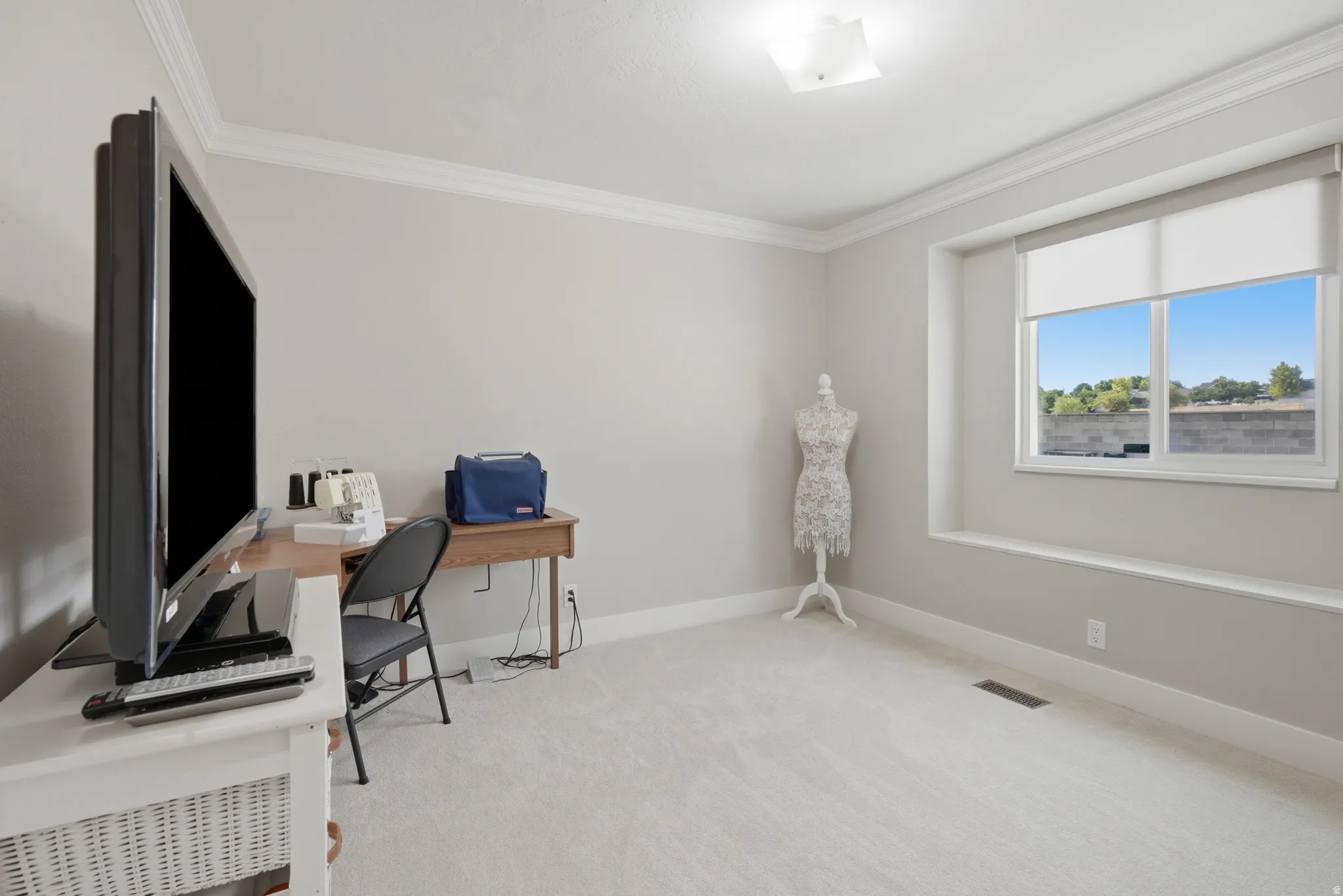 Bright room featuring a large window with roller shades, light grey carpeting, white baseboards, and crown molding