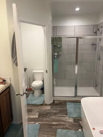 Bathroom featuring a glass-enclosed shower with tile surround, a freestanding tub, and wood-finish flooring