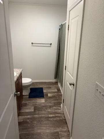 Bathroom featuring wood-finish flooring, a dark wood-tone vanity with a light countertop, and a shower with an opaque curtain