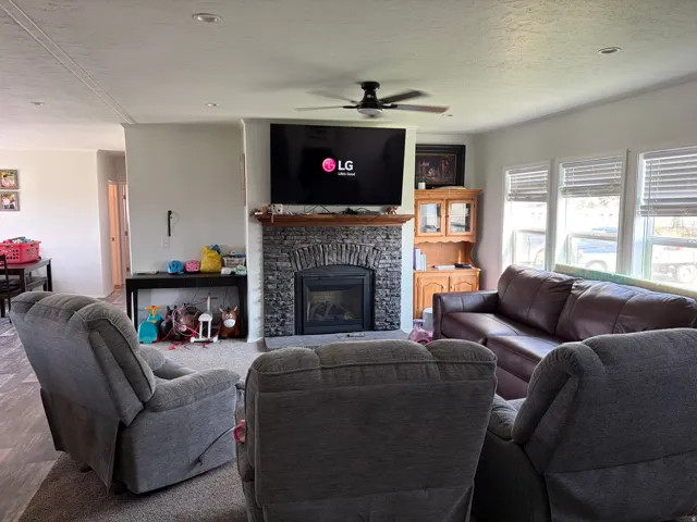 Living area featuring a stone-clad fireplace with a wood mantel, a ceiling fan, recessed lighting, and multiple windows with blinds