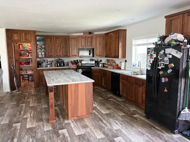 Spacious kitchen featuring warm wood cabinetry, a central island with a stone-finish countertop, and wood-finish flooring