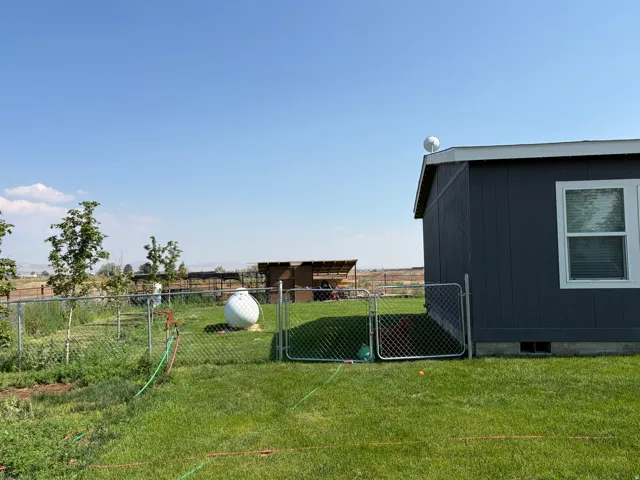 Expansive rear yard featuring green lawn, chain-link fencing, and mature trees