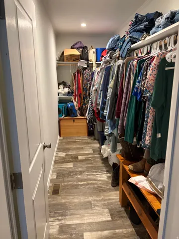 Spacious walk-in closet featuring wood-finish flooring, recessed lighting, and extensive built-in shelving and hanging rods for organization