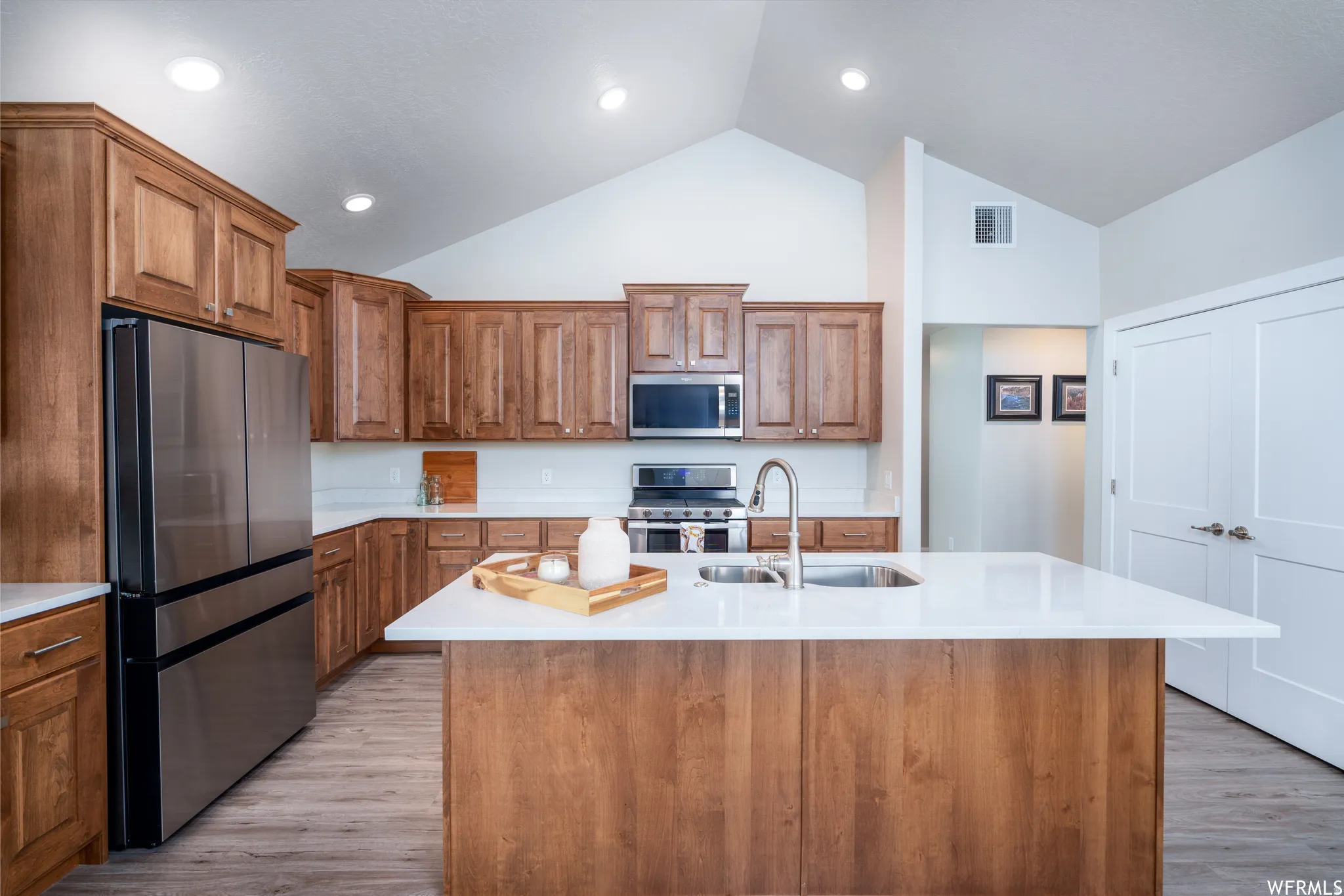 Kitchen featuring a central island with an undermount sink, stainless steel appliances, wood-finish cabinetry, vaulted ceilings, and recessed lighting