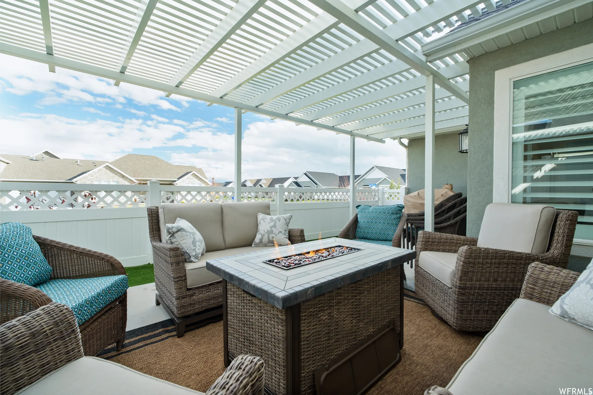 Patio featuring a lattice pergola, built-in fire pit with tile surround, stucco exterior, and white privacy fencing