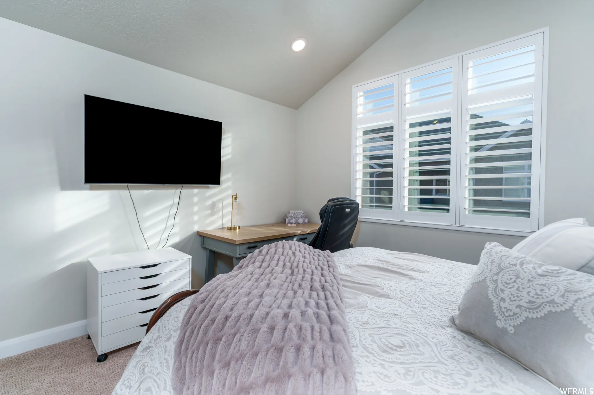 Vaulted ceiling bedroom featuring white plantation shutters, neutral wall tones, and carpet flooring