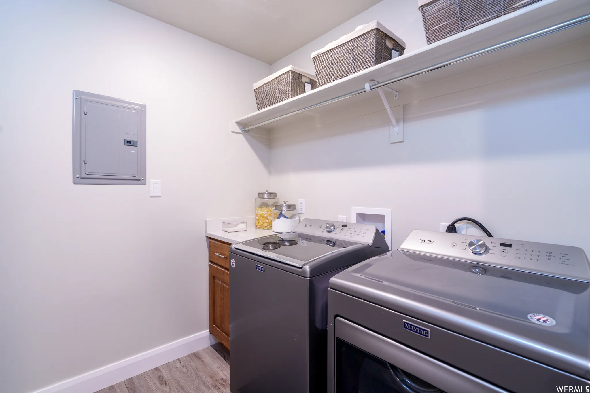 Dedicated laundry space featuring wood-finish flooring, light cabinetry with a solid surface countertop, and an integrated shelf with a hanging rod