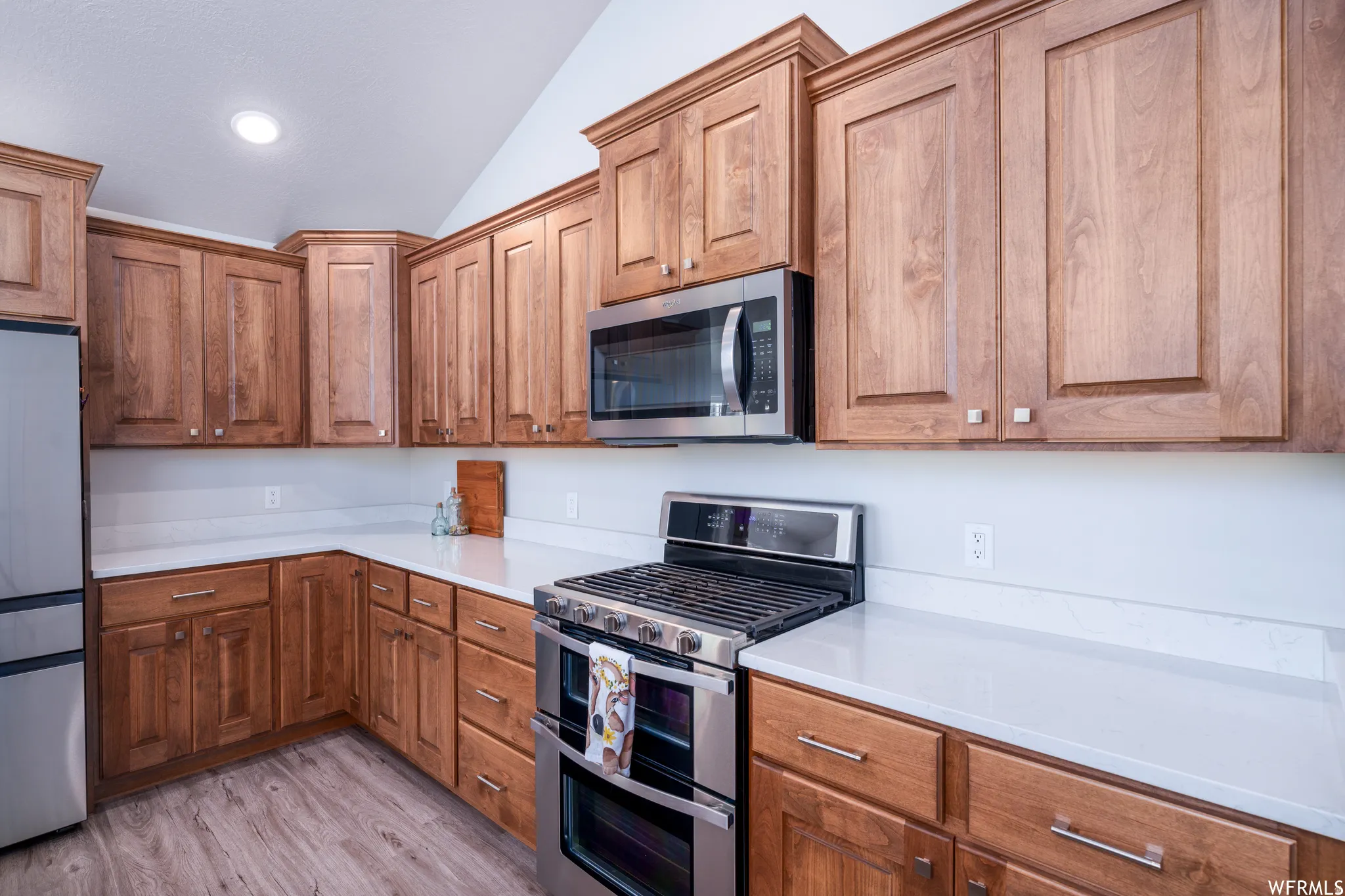 Kitchen featuring warm wood cabinetry, stainless steel appliances, solid surface countertops, a gas range with double ovens, and wood-finish flooring