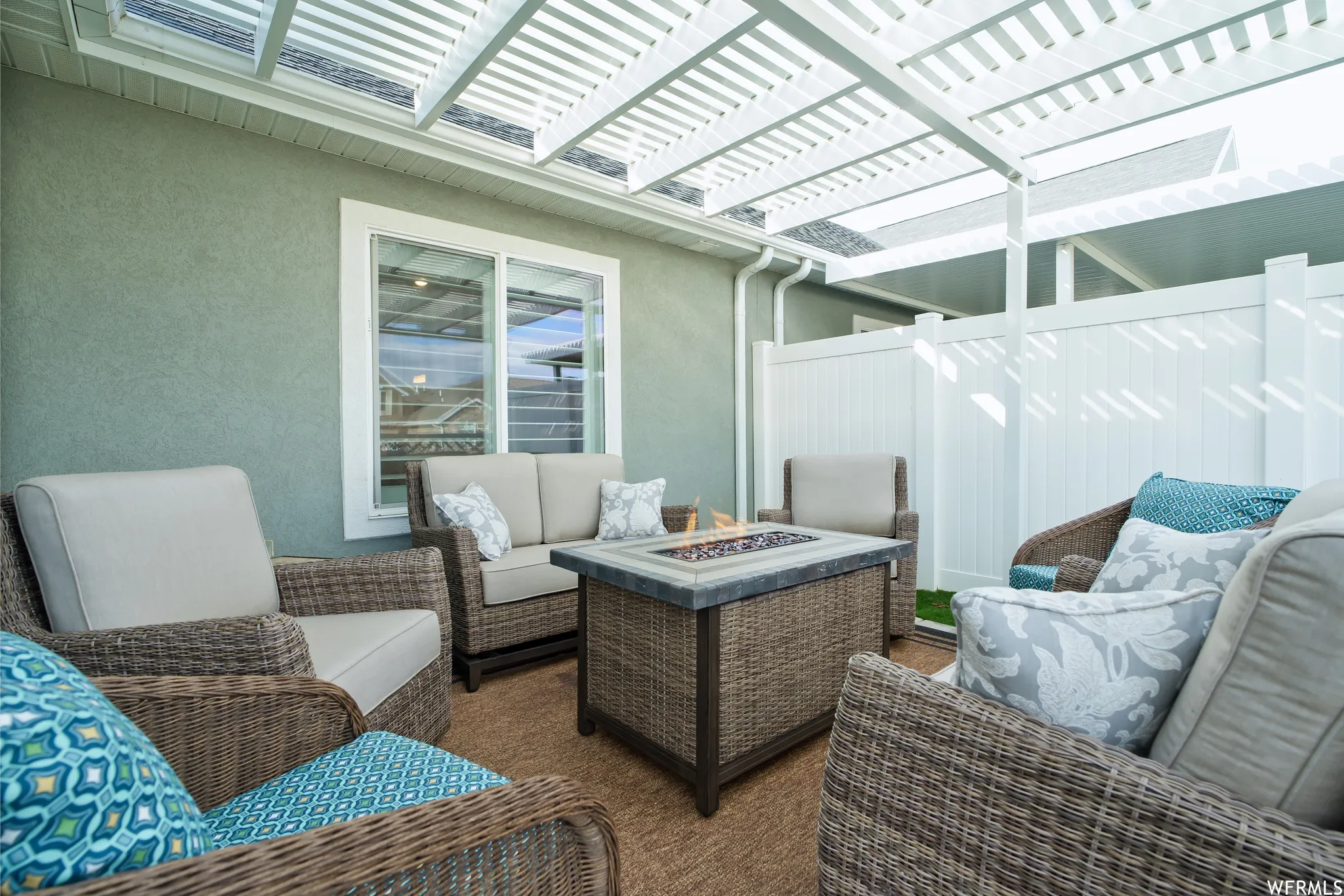 Patio area featuring a white slatted pergola, stucco exterior wall, and privacy fencing