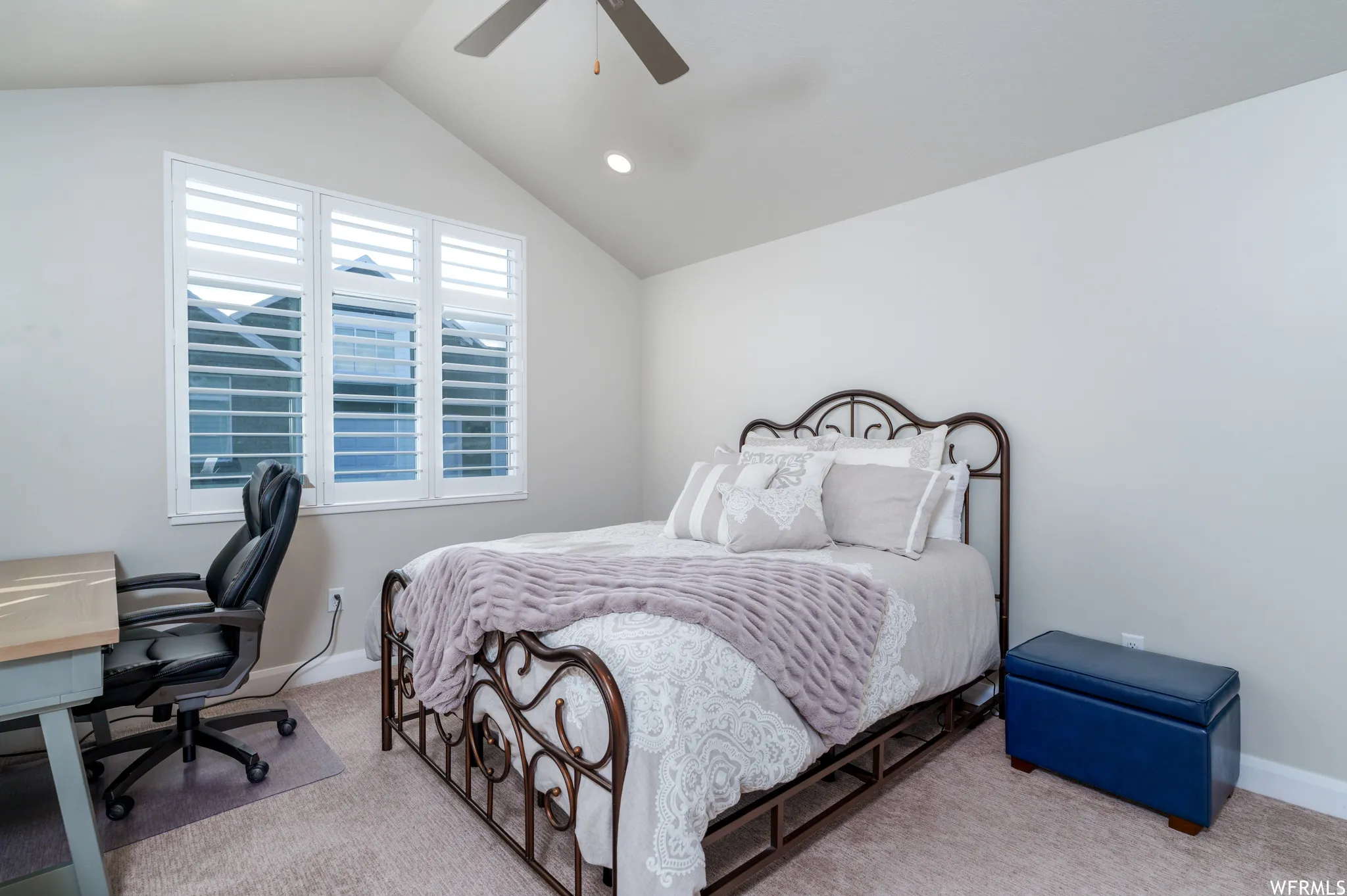 Vaulted ceiling bedroom featuring triple windows with white plantation shutters, neutral carpeting, and a ceiling fan
