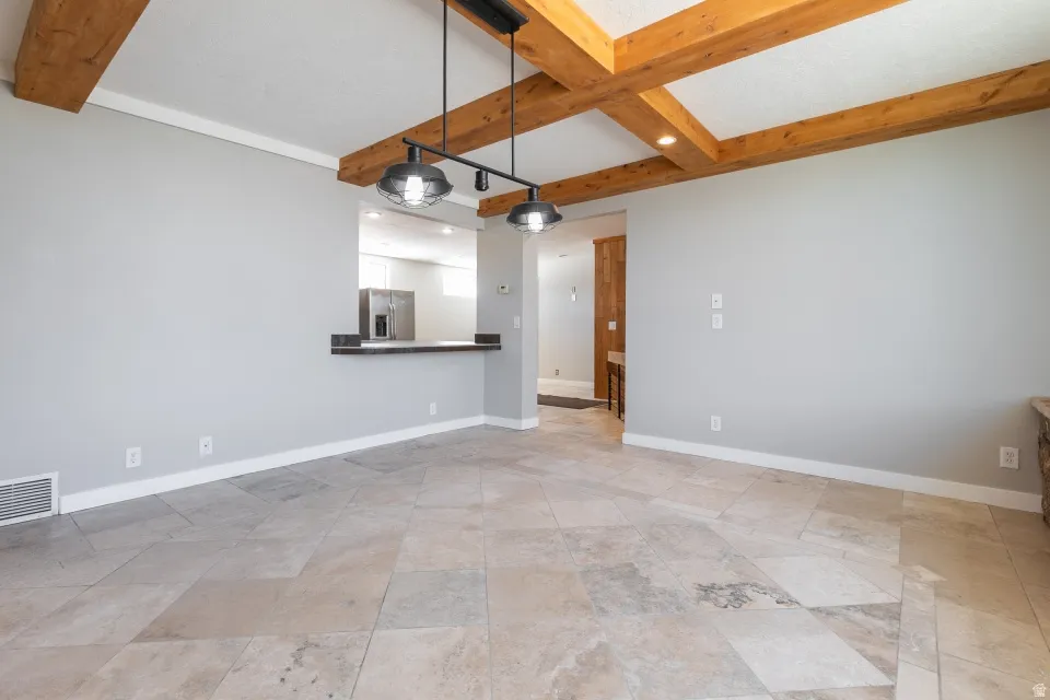 Vaulted ceiling with exposed wood beams, large format floor tile, pass-through window with dark countertop, and modern industrial-style pendant lighting