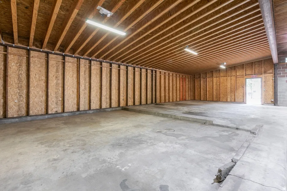 Spacious commercial interior featuring exposed wood ceiling joists, concrete flooring, and fluorescent lighting fixtures