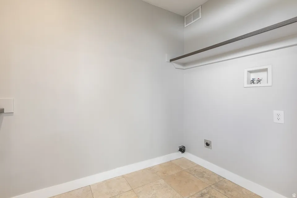 Laundry area featuring light-colored tile flooring, white baseboards, and a wall-mounted clothing rod