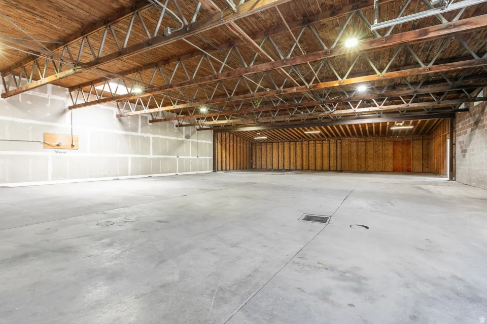 Expansive open industrial space featuring a concrete floor, exposed wood beam ceiling, metal truss system, and recessed lighting