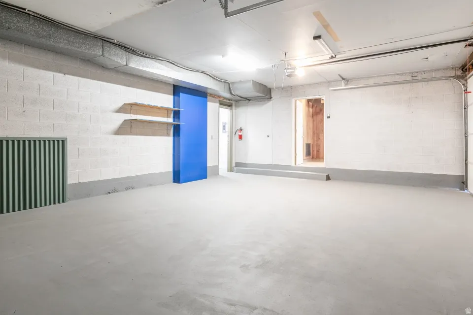 Spacious garage featuring concrete block walls, a durable concrete floor, and exposed overhead ductwork