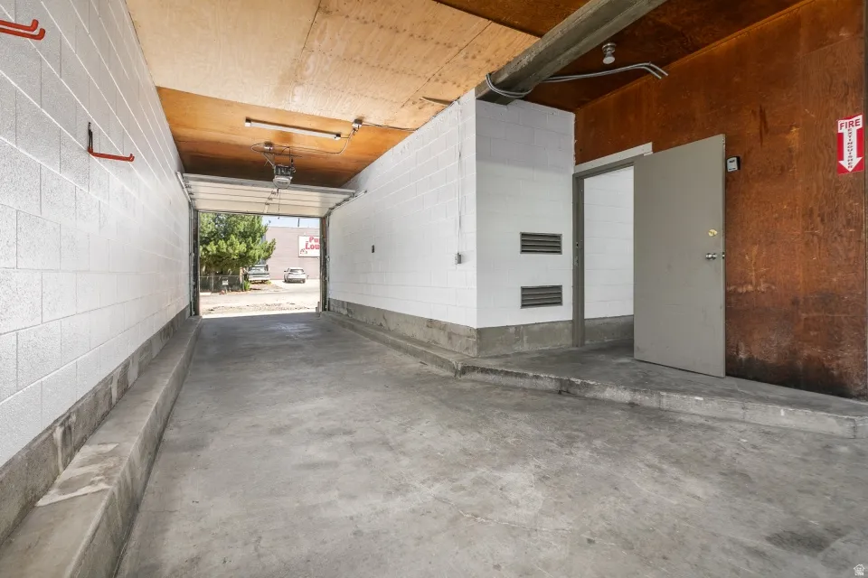 Concrete floor garage with high ceilings, an overhead garage door, interior metal door, and block wall construction