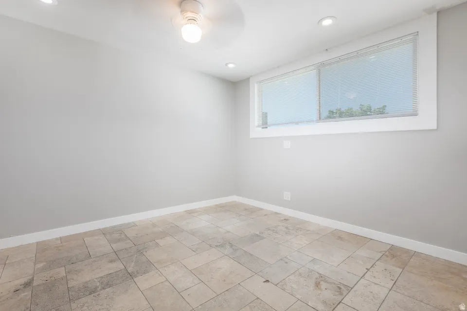 Room featuring light gray walls, large rectangular window with white trim, recessed lighting, and a ceiling fan with integrated light