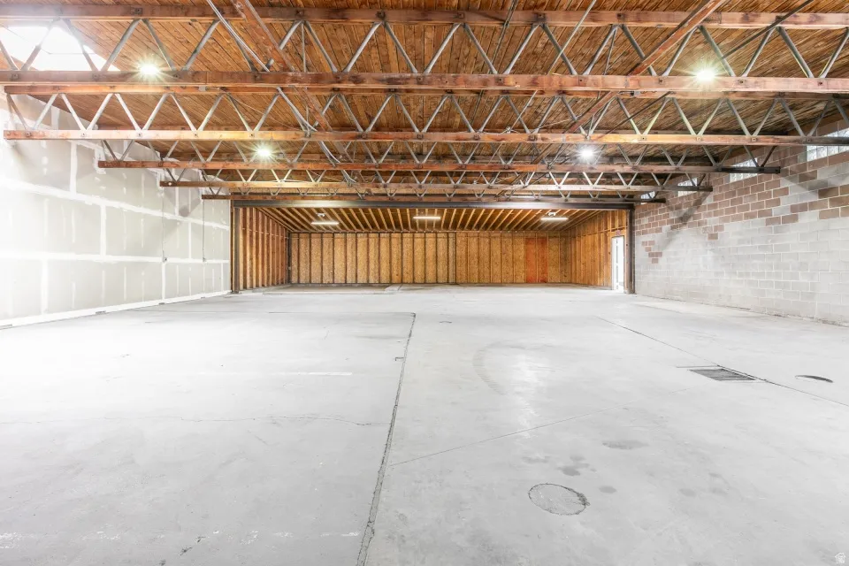 Spacious interior featuring exposed wooden ceiling trusses, concrete flooring, drywall-ready walls, and brick/block wall construction