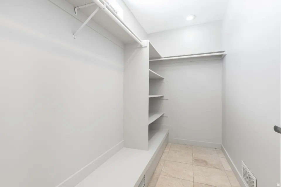 Walk-in closet featuring built-in shelving, hanging rods, and light-toned tile flooring
