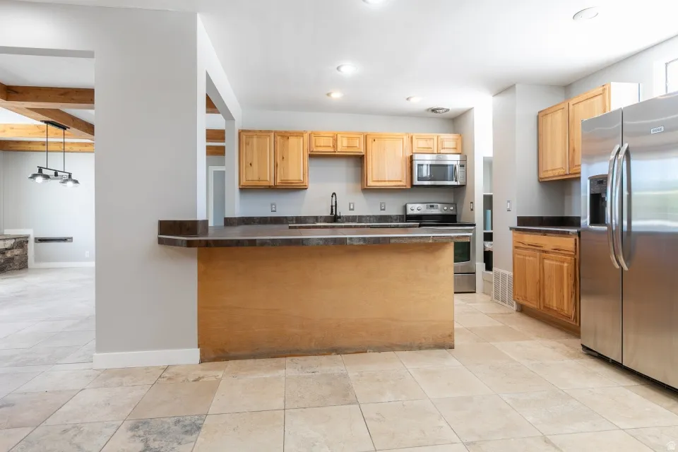 Kitchen with light wood cabinetry, dark countertops, and stainless steel appliances