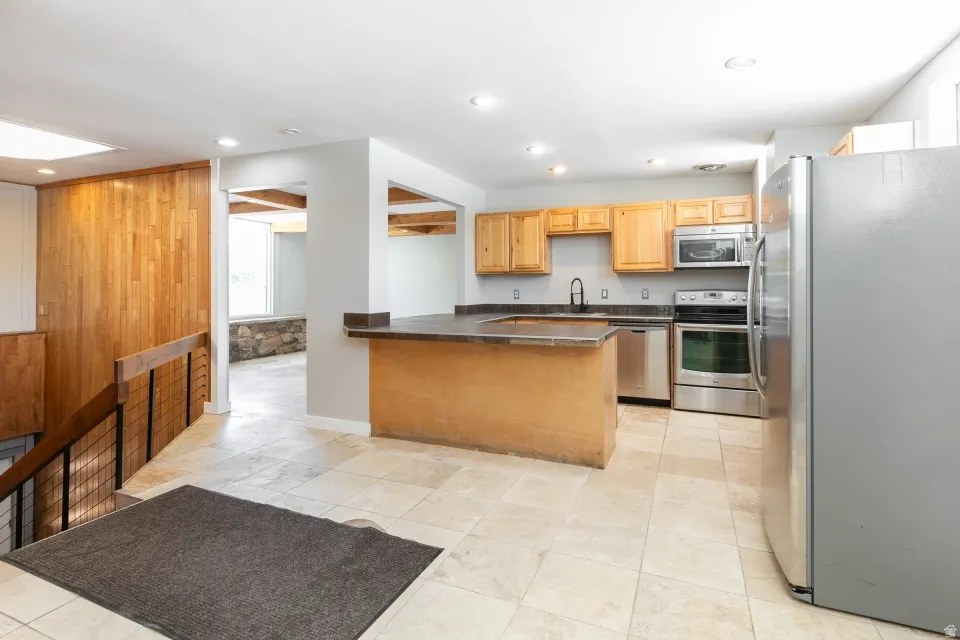 Kitchen featuring light wood cabinetry, stainless steel appliances, dark countertops, and a peninsula with a breakfast bar