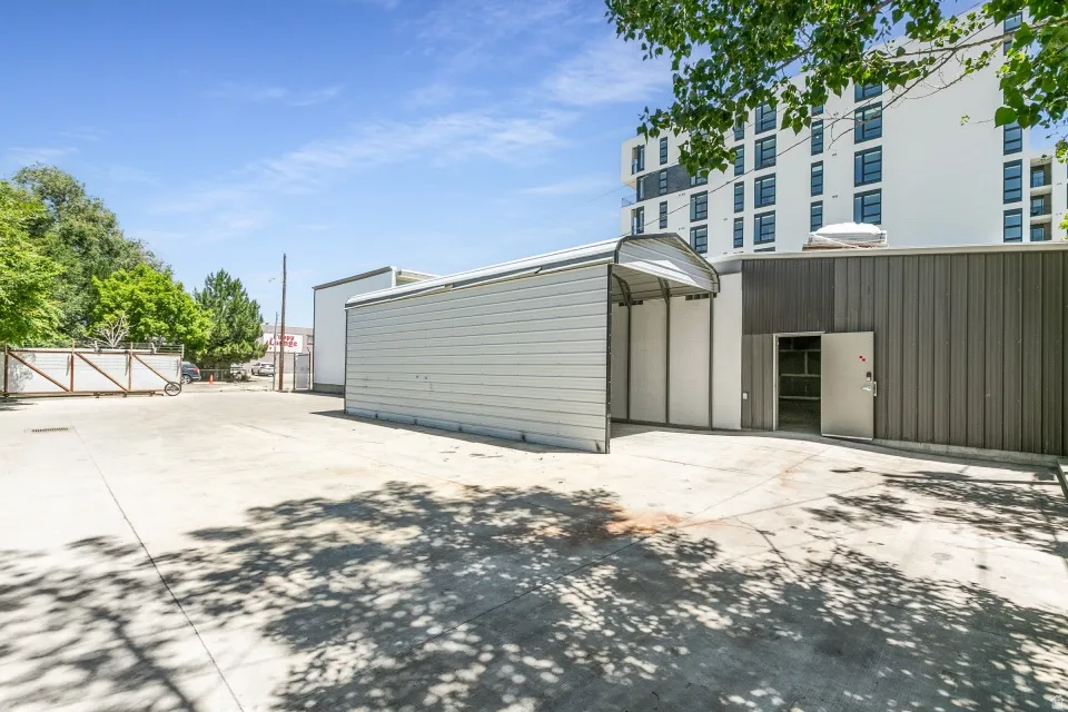 Expansive concrete pad featuring a metal carport structure and a corrugated metal building with an open doorway