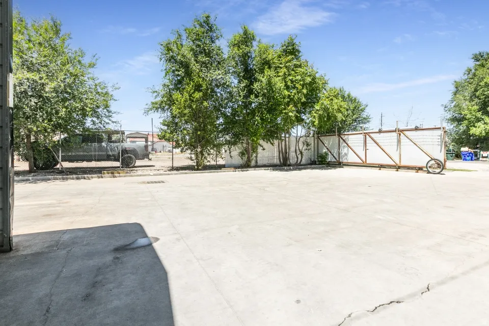 Expansive concrete lot with a chain-link fence and mature trees