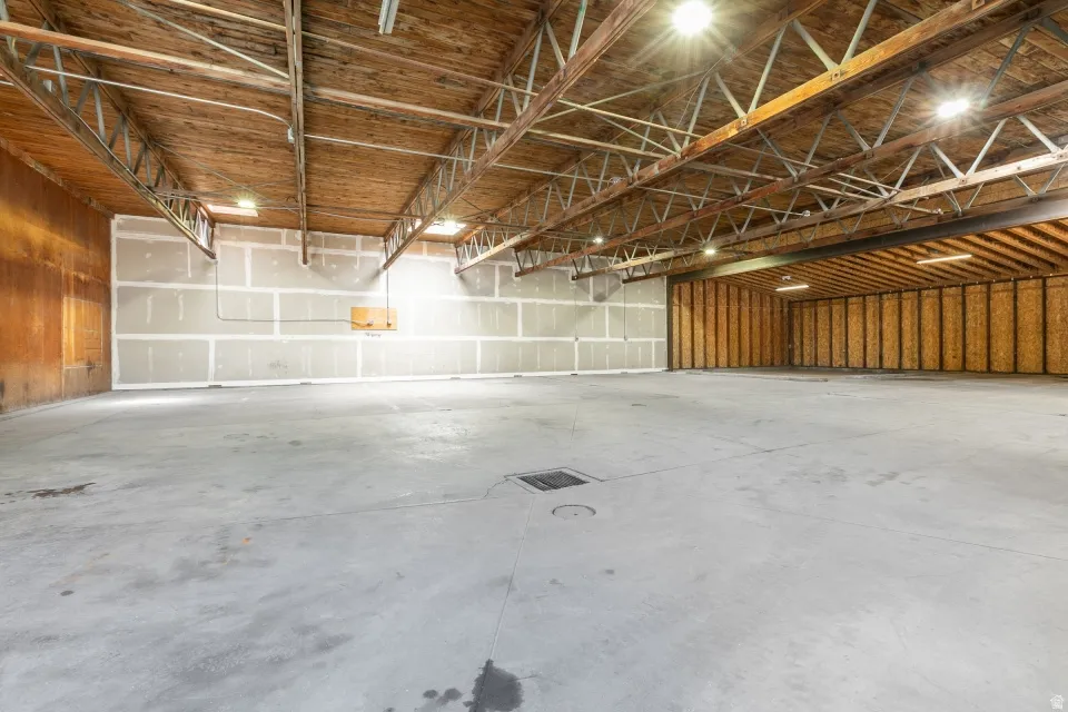 Expansive interior space featuring concrete flooring, exposed wood beam ceiling with metal trusses, recessed lighting, and mixed wall finishes including wood paneling and unfinished drywall sections