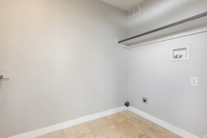 Laundry area featuring light-colored tile flooring, white baseboards, and a wall-mounted clothing rod